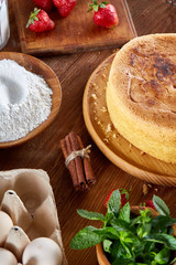 Baking background with strawberry tart covered with whipped sour cream, ingredients over wooden background.
