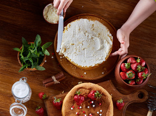 Close up of girl's hands adding cream on top of delicious strawberry cake, close up, selective focus.