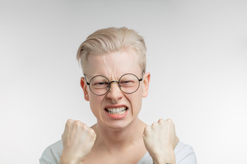 Headshot of enraged blonde man in spectacles looking at the camera with clenched fists with...
