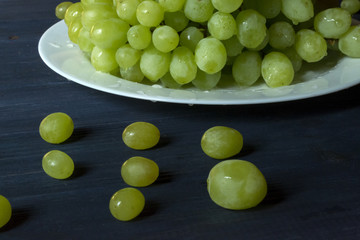 Ripe grapes in a plate on a dark blue wooden table.