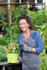 Naklejka na ściany i meble Fröhlich lächelnde Mitarbeiterin im Gartencenter mit einer Tomatenpflanze im Topf
