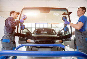 Automobile special workers replacing windscreen or windshield of a car in auto service station...