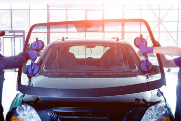Automobile special workers replacing windscreen or windshield of a car in auto service station...