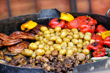 Frying pan with fried potatoes, sausages, mushrooms and pepper.Street food and outdoor cooking concept.