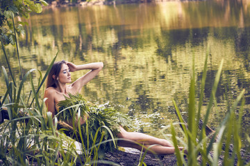 Summer heat. Beautiful young girl in a forest lake, open clothes from fern leaves, perfectly combined with nature. A person in the form of a fantasy elf, dryads, cosplay of a character.