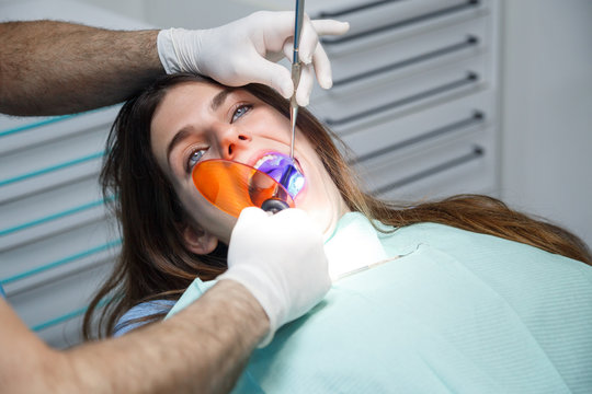 Crop view of hands of dentist in gloves doing filling of tooth to young female.  