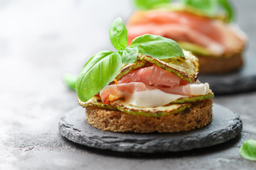 Mini ham  (hamon, prosciutto) sandwiches, fried zucchini and Basil close-up on black surface....