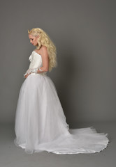 Fototapeta premium full length portrait of blonde girl wearing white fantasy gown. standing pose in side profile, grey studio background.