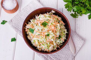 Fresh coleslaw salad in bowl on white wooden background.