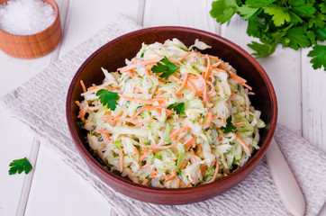 Fresh coleslaw salad in bowl on white wooden background.