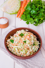 Fresh coleslaw salad in bowl on white wooden background.