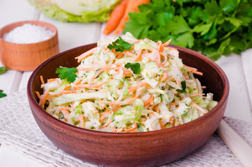 Fresh coleslaw salad in bowl on white wooden background.