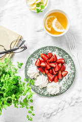 Breakfast or snack table - fresh strawberries, meringue, green tea with lemon. Cozy home still life on a light background, top view