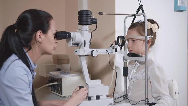 Female ophthalmologist is checking vision of school girl using microscope and slit lamp. Doctor is using biomicroscopy of eye in clinic, modern equipment
