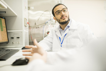Naklejka premium Group of highly professional technicians wearing lab coats gathered together in front of computer and studying data, interior of modern pressure transducers factory on background