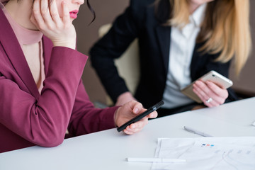 technology addiction. business women using their phones at office meeting. idle life and work style.