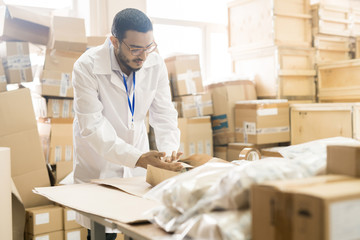 Handsome Arabian worker wearing lab coat preparing production lot for delivery while working at...