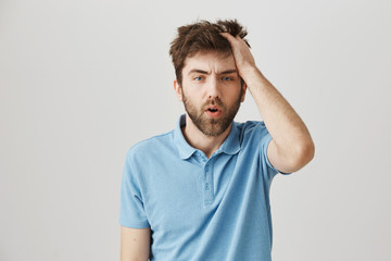 Fototapeta na wymiar Funny mature bearded man with messy hair and beard, rubbing head and being tired or having hangover, standing over gray background. Confused and sleepy guy after celebrating b-day with fellows