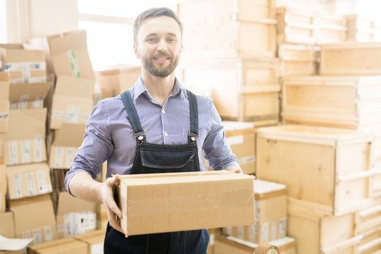 Waist-up portrait of handsome middle-aged warehouse worker holding cardboard box in hands and posing for photography