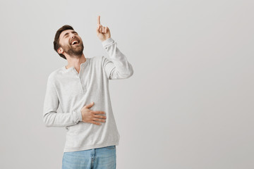 Joyful emotive young european male bending backwards while laughing out loud and holding belly,...