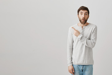 Fototapeta premium Have you seen what happened there. Portrait of interested excited handsome man with beard pointing left or behind while expressing surprise and shock after hearing intriguing rumor