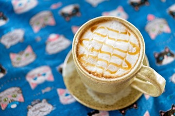glass of hot caramel macchiato coffee is topped by a dense creamy foam and caramel sauce on table. top view and copy space with vintage background