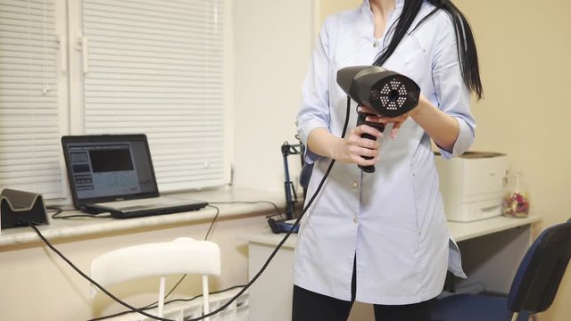 Professional ophthalmologist in holding special device for eye testing indoor. Connected to laptop. Adjusting device.