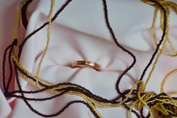 Gold ring and colored beads are on a light fabric.