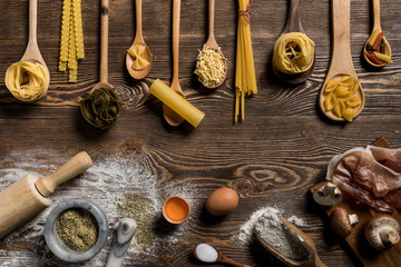 Raw pasta on wooden spoons on wooden table.