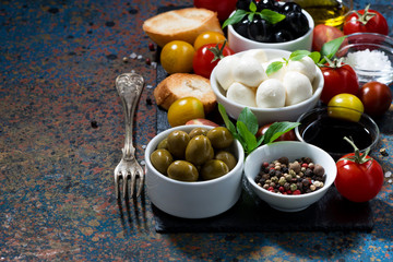 mozzarella, ingredients for the salad and bread on dark background, closeup