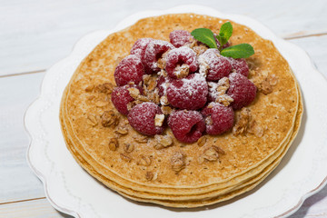 traditional thin pancakes with fresh raspberries on plate on wooden table, closeup