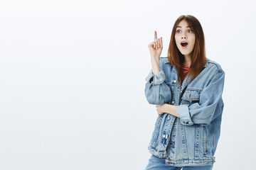 Girl finally understood something. Upbeat good-looking urban female student in denim jacket, raising index finger up in eureka gesture, opening mouth with got it, being glad to find answer