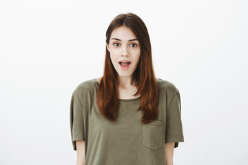 Fototapeta premium Excited woman heard amazing unbelievable rumor about her promotion. Studio shot of intrigued beautiful caucasian female with brown hair in t-shirt, opening mouth and gazing focused at camera