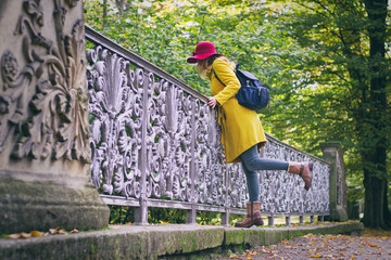 Beautiful woman is wearing woolen coat and red hat. Tourist woman standing on bridge in public park...
