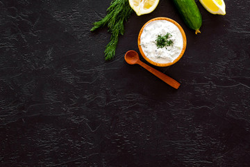 Greek yogurt dip with greenery, cucumber, oranges, garlic on black background top view copy space