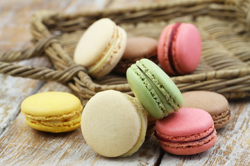 Colorful French macaroons scattered around on wooden and wicker surface
