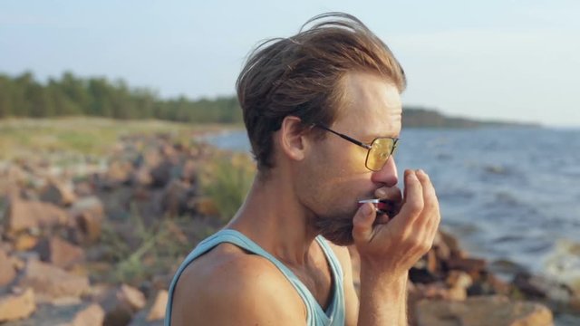 Young man in shirt and sunglasses playing on the harmonica on the coast.
