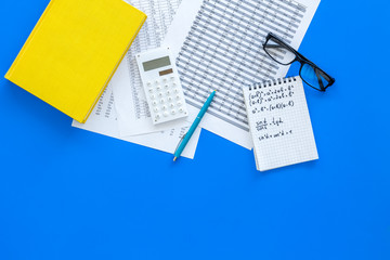 Math homework. Math textbook or tutorial near sheet with numbers, countes, calculator, notebook with formula on blue background top view copy space