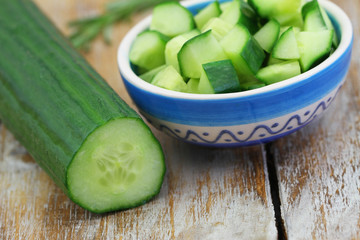 Fresh cucumber with cucumber salad in bowl on rustic wooden surface


