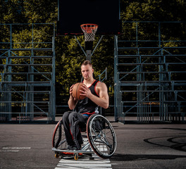 Cripple basketball player in a wheelchair holds a ball on an open gaming ground.
