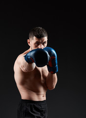 Fototapeta na wymiar Low key studio portrait of handsome muscular fighter practicing boxing on dark blurred background