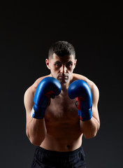 Plakat Low key studio portrait of handsome muscular fighter practicing boxing on dark blurred background