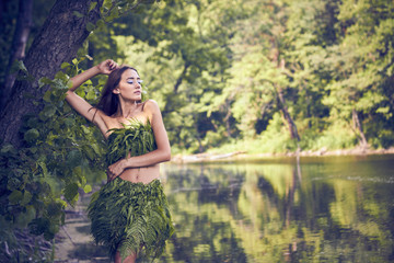 Summer heat. Beautiful young girl in a forest lake, open clothes from fern leaves, perfectly...
