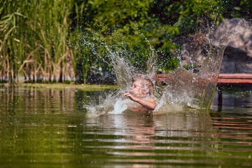 Young boy jumping, swimming and splashing in the river on summertime