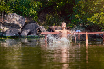 Fototapeta na wymiar Young boy jumping, swimming and splashing in the river on summertime