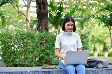 Business Concepts. Young Asian businesswoman working in the garden. Beautiful girl playing computer in the garden.