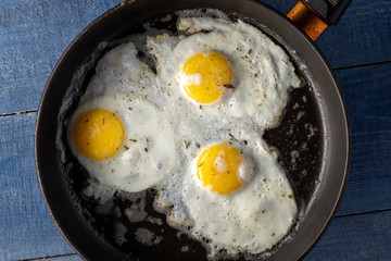 Fried eggs with seasoning on the pan on blue wooden table. top-view