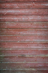 Fototapeta premium Full frame background of an old and faded wood board wall painted in red with vignette