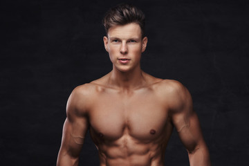 Fototapeta na wymiar Close-up portrait of a sexy shirtless young man model with a muscular body and stylish haircut posing at a studio. Isolated on dark background.