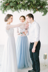 Beautiful smiling master of wedding ceremony holding glass box with wedding rings. The groom is wearing bride's ring on her finger and kissing her hand.